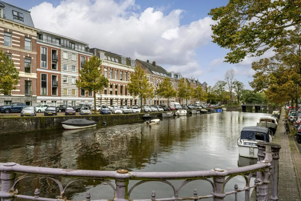 Uitzicht op de Nieuwe Gracht in Utrecht met geparkeerde boten, auto's en statige herenhuizen langs het water.